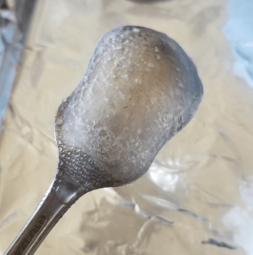 A close-up photo of the back of a silver serving spoon with a webbing of wax collected on it.
