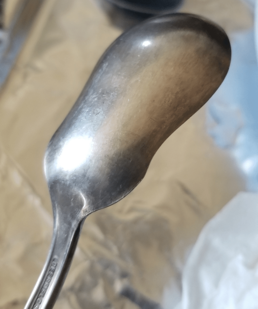 A close-up photo of the back of a silver serving spoon.