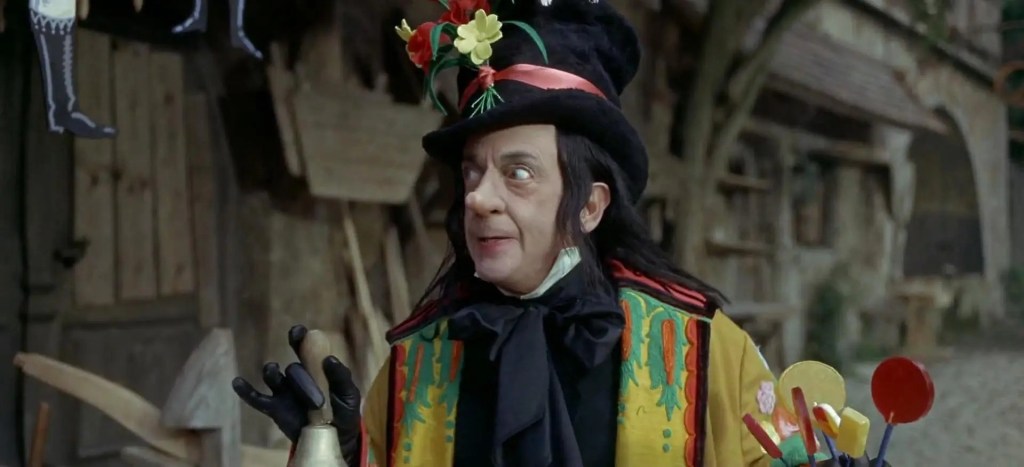 Screencap from the movie Chitty Chitty Bang Bang of the Child Catcher. A person in black, with bright colors artificially added, holds a bell and a handful of tempting lollipops while side-eyeing a building that children are totally hiding in. 