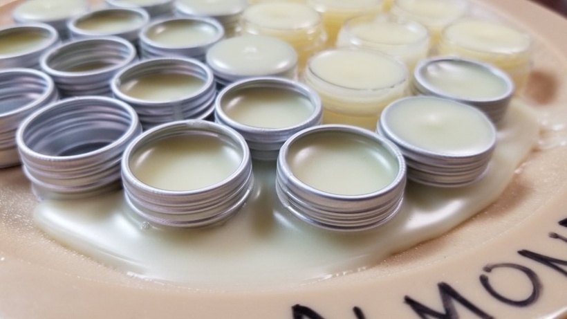 A close-up photograph of almond lip balm HORRIBLY MISPOURED on and around twenty-ish empty containers on a plate.