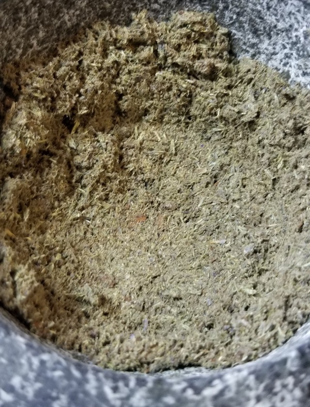 Close up photograph of powdered cloves and lavender flowers in the bowl of a granite mortar.