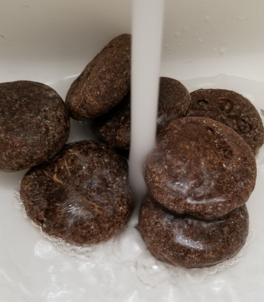 Photo of several falafel-shaped soaps under a full stream of running sink water.
