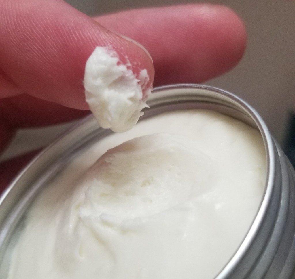 Photograph of a white, rosewater cold cream in a tin. It has the appearance of a whipped body butter or frosting.