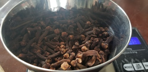 Photograph of a metal bowl of whole cloves on a digital scale.
