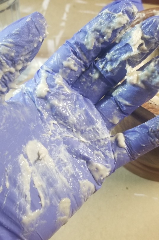 Photograph of a latex-gloved hand, covering in messy soap goo.