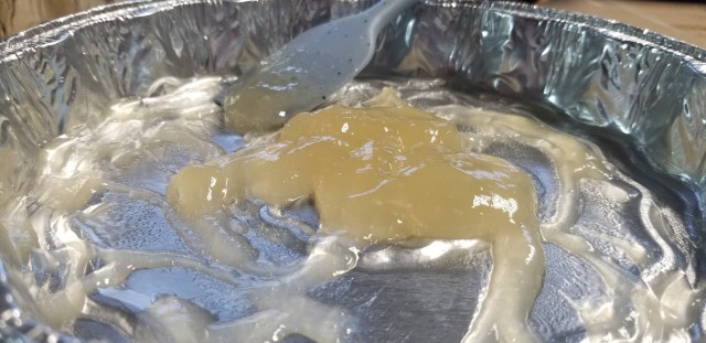 Closeup photograph of a disposable tin pie plate with a thick, slimy golden goo gathered together in the center by a hapless spatula resting along the back.