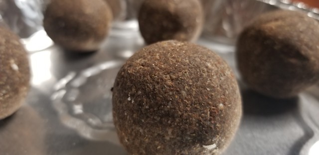 A close-up photograph of dried, brown, speckled balls of soap in an aluminum tin.