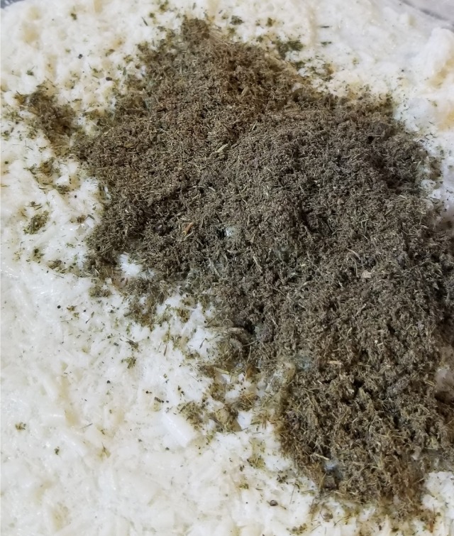 Close up photograph of powdered lavender and cloves poured over a dampened, somewhat reconstituted-mashed-potato-like tray of soap.