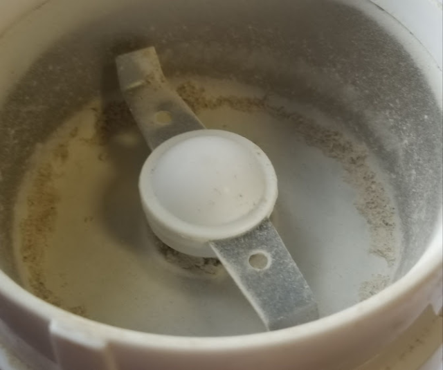 Close up of the grinding chamber of an inexpensive electric coffee grinder. There is a fine green-grey powder clinging to the edges.