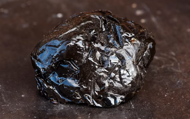 Photograph of a fairly disgusting looking spheroid of brown resin, looking as if it has spent rather too long being imprinted with the insides of a plastic bag.