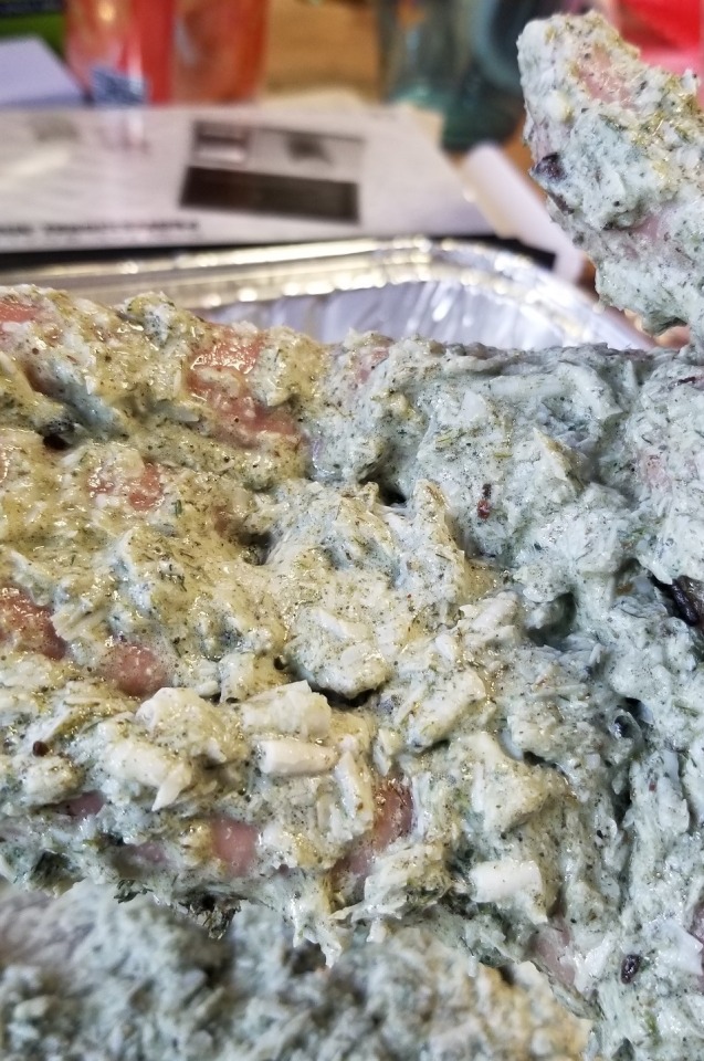 Close up photograph of a hand covered in mixed choppy green goo.