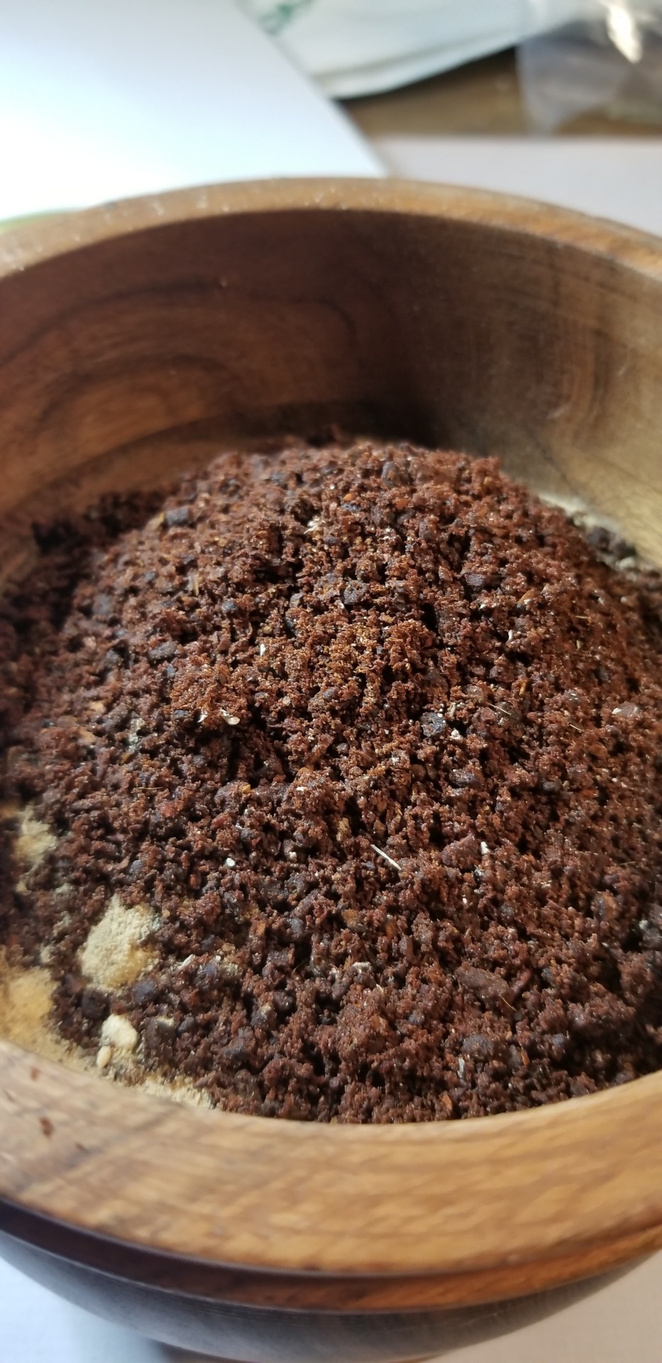 A photograph of a mortar very full of various powders, the topmost of which is an oily, rich-looking dark brown pile of ground cloves.