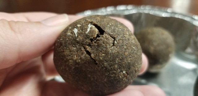 A close-up photograph a hand holding up a brown ball of soap with a significant crack.