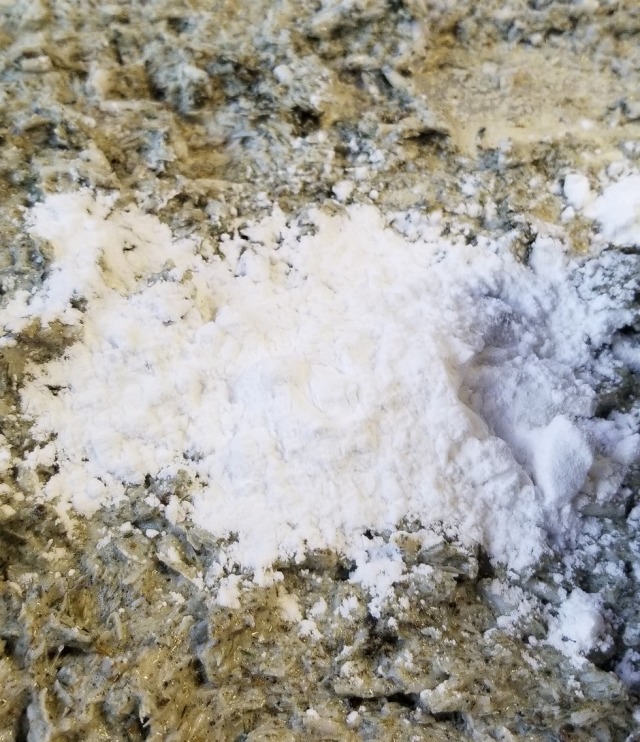 Closeup photograph of a large pile of white arrowroot powder dumped onto a mass of green soap mix.