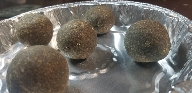A photograph of an aluminum tin with five brown, speckled, rounded balls of soap, slightly shiny in the light.